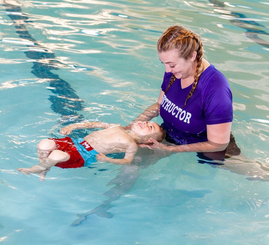 female-instructor-teaching-smiling-boy-to-float-in-water-1